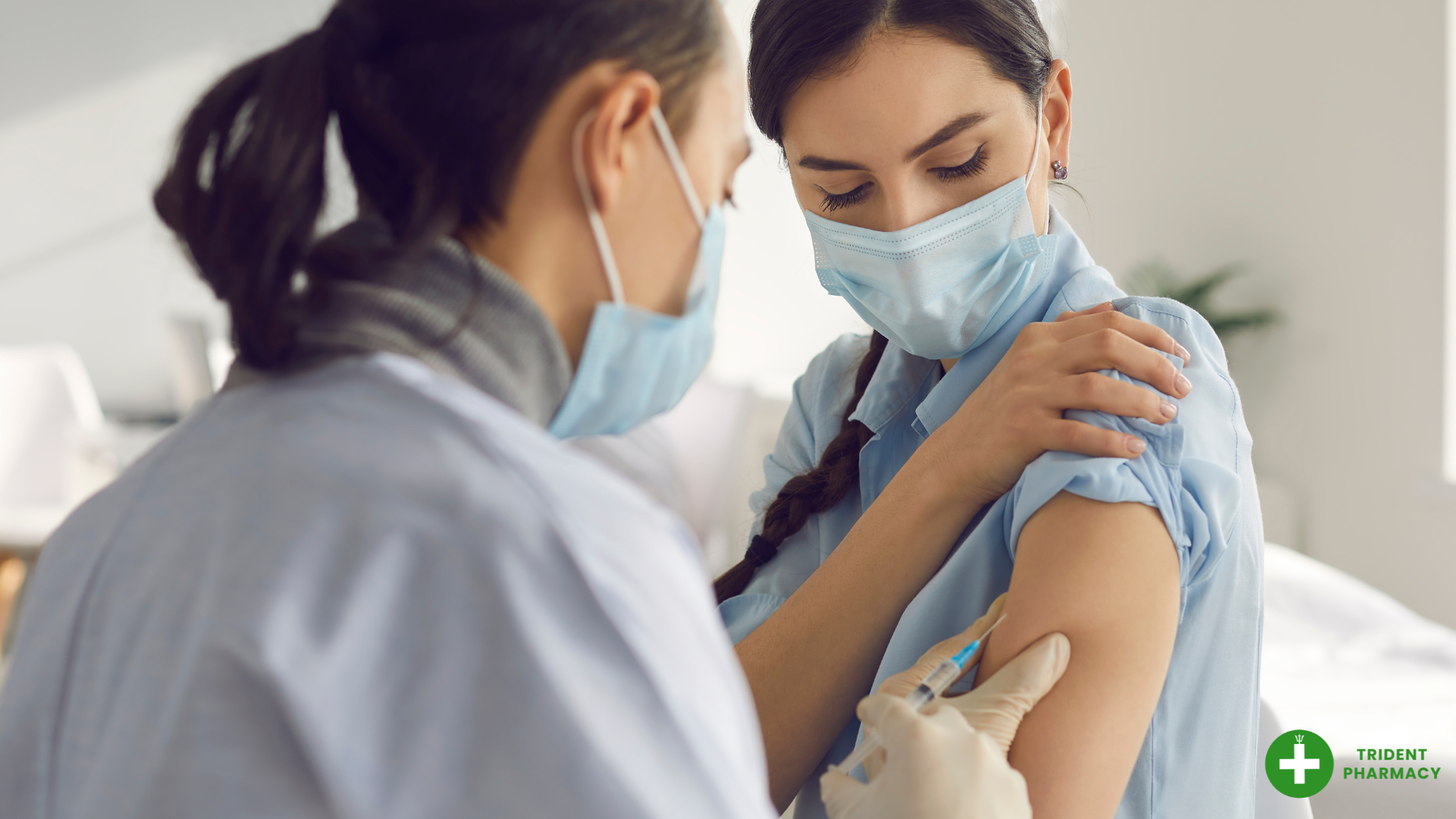 A healthcare professional administering a COVID-19 vaccination to a woman wearing a face mask at Trident Pharmacy. The patient is seated and lifting her sleeve to receive the injection, promoting safety and care during the vaccination.
